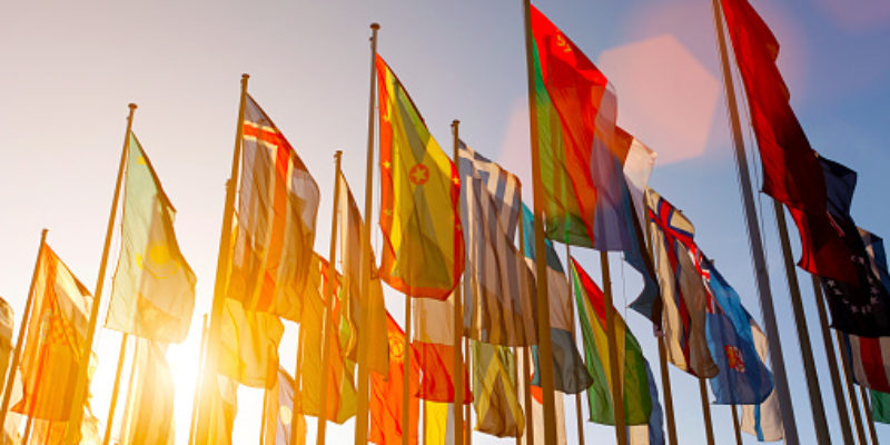 Group of many colorful internationl world flags waving in the sky at sunset, with shining sun and lens flare, low angle view.